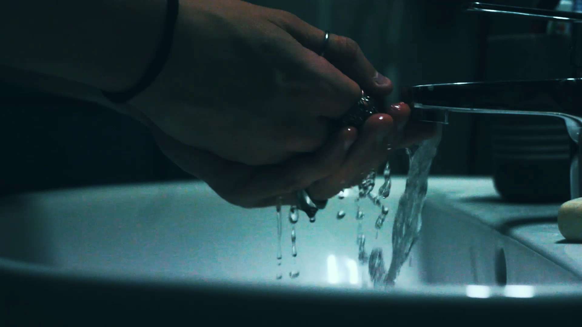 Photo d'une main qui prend de l'eau au dessus d'un lavabo, avec une vue de profil