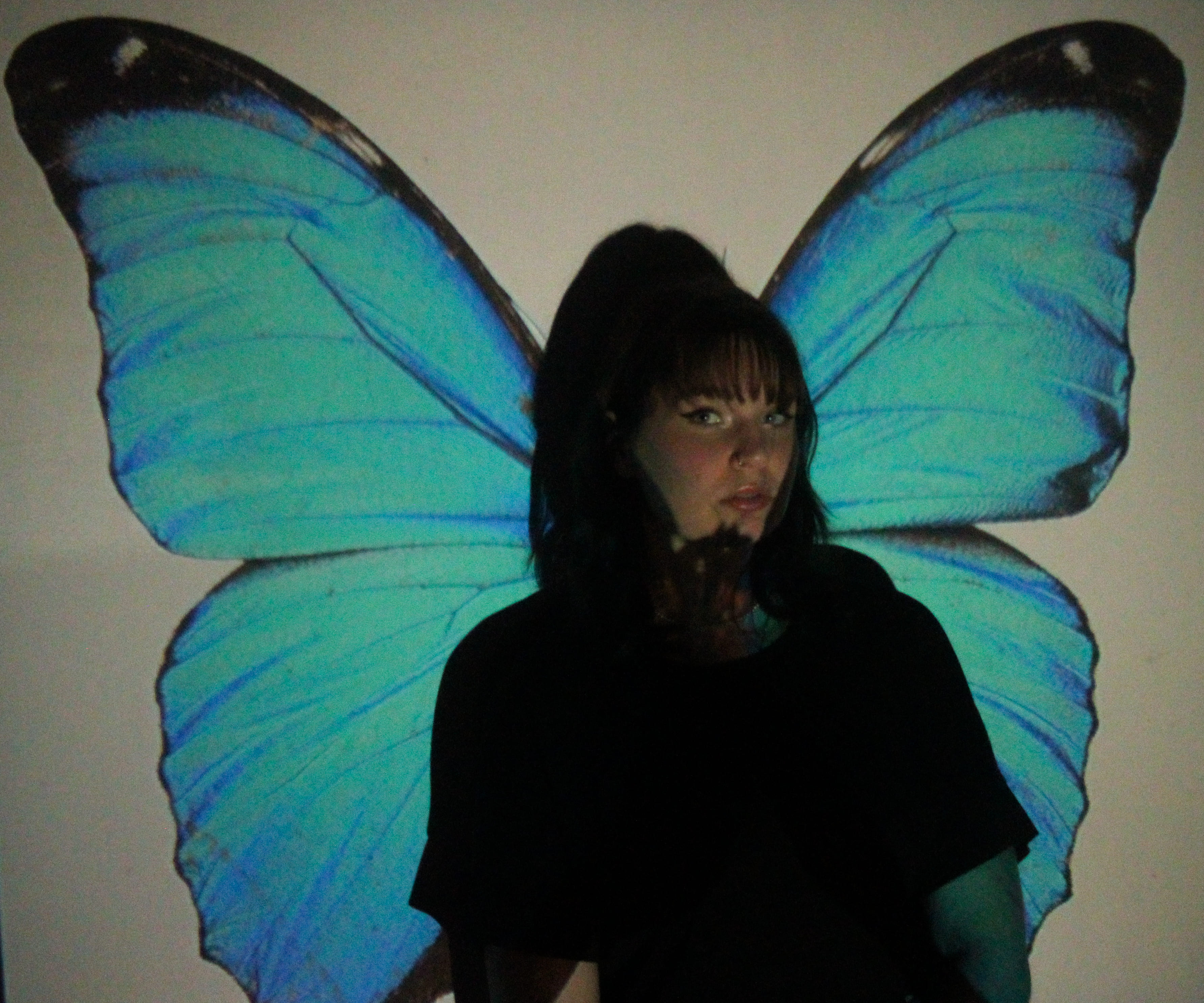 Photo d'une femme assise devant un projecteur qui projete une image de papillon, les ailes s'attachant a la femme